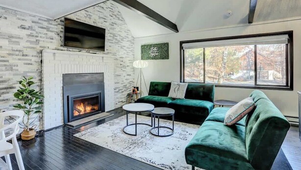 Una sala de estar moderna con chimenea, sofá verde y un ventanal grande.