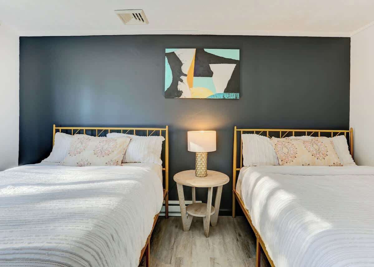 Hotellihuone, jossa on kaksi sänkyä, pyöreä pöytä lampun kanssa ja seinätaideteos.