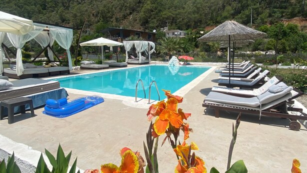 Uma área de piscina com espreguiçadeiras e guarda-sóis, rodeada por vegetação e colinas.