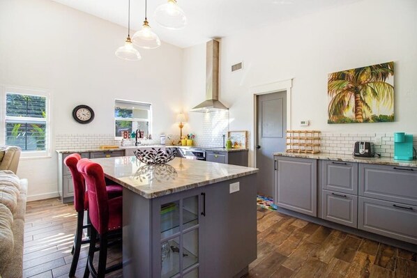 A modern kitchen with a central island, grey cabinets, and a large window.