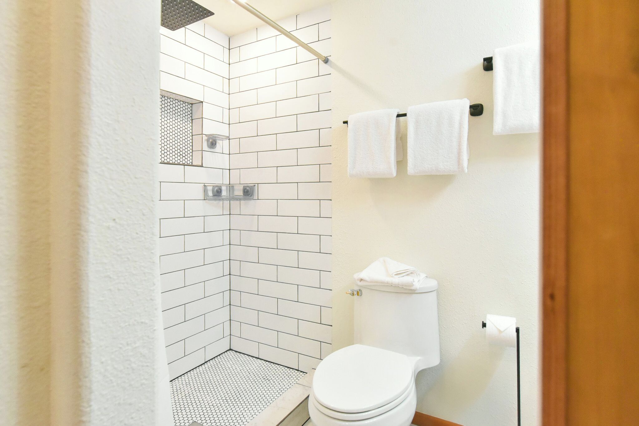Une salle de bain avec des murs recouverts de carreaux blancs, des toilettes blanches et un espace douche.
