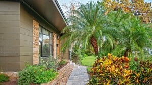 A modern house with a stone facade, a paved pathway, and lush tropical plants.