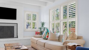 A living room with a beige sofa, a wooden coffee table, and a TV mounted on a white brick wall.
