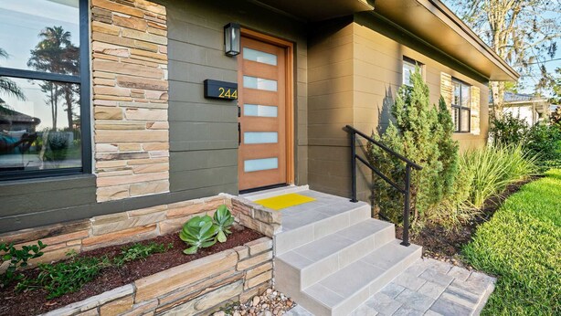 A modern house with a stone facade, a wooden door, and a number '244' above it.