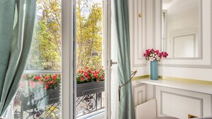 Una stanza con vista su alberi e fiori visibili attraverso una porta aperta, un vaso con fiori su uno scaffale, e una bicicletta all'esterno.