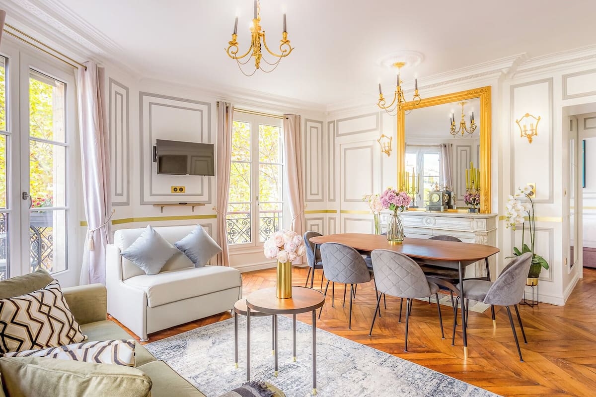 A spacious living room with a sofa, dining table, chairs, and a TV.
