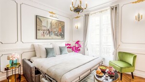 Una camera d'albergo con un letto, una poltrona verde, un tavolo imbandito per la colazione e un quadro appeso al muro.