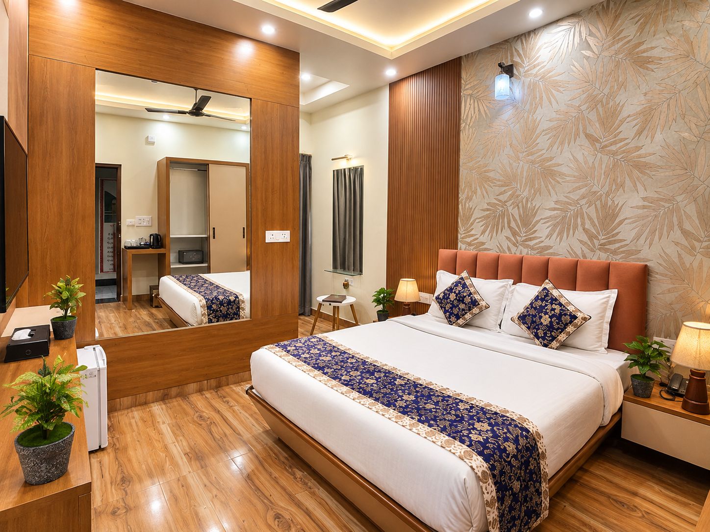 Habitación de hotel con una cama grande, un espejo, un armario de madera, una mesita de noche con una lámpara y una pared con diseño de hojas.