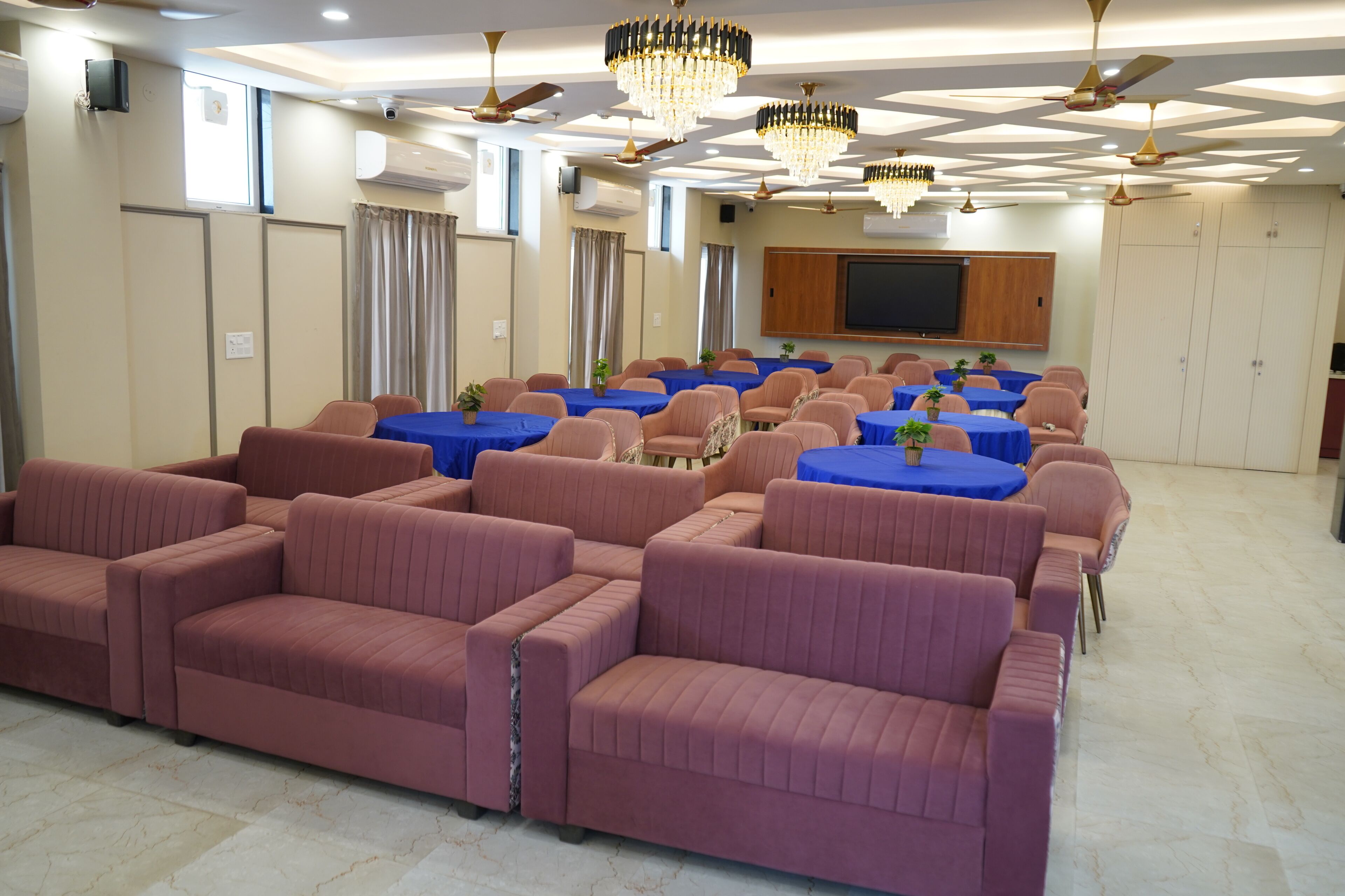 A conference room with rows of sofas and tables, ceiling fans, and a flat-screen TV.
