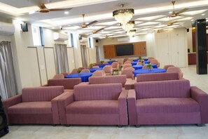 Une salle de conférence avec des rangées de chaises, un grand écran et des ventilateurs de plafond.