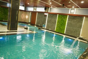 Une piscine intérieure à l’eau claire, dotée d’un plongeoir et d’un plafond avec des lambris en bois et des luminaires encastrés.