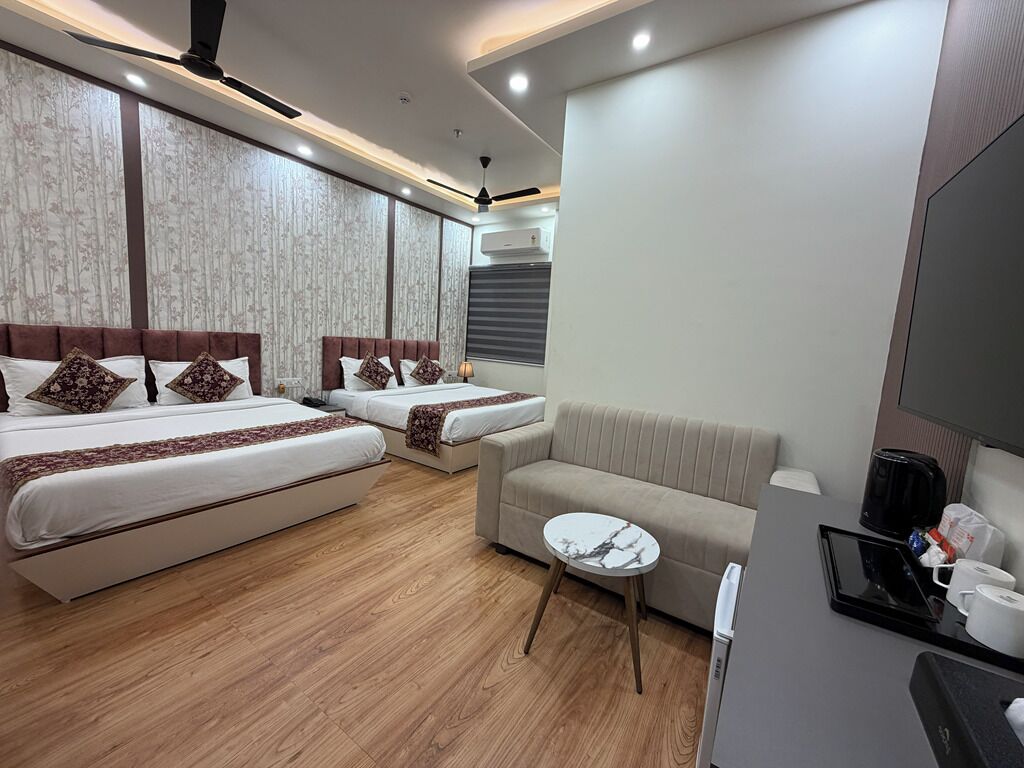 A hotel room with two beds, a sofa, a small round table, and a flat-screen TV.