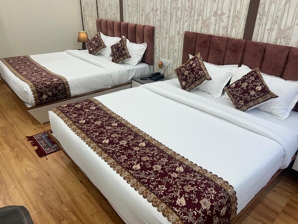 Habitació d'hotel amb dos llits, cada un amb un llençol i coixins estampats vermells i daurats. La habitació té terres de fusta i una petita catifes.