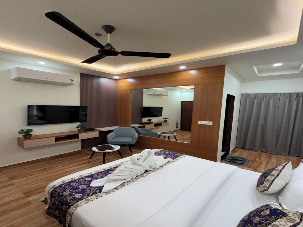 Quarto de hotel moderno com cama, escrivaninha, cadeira, televisão e ventoinha no teto.