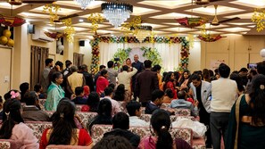A crowded indoor event with floral decorations and chandeliers. - Aanchal Palace Hotel  (Jaipur)
