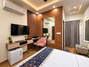A hotel room with a bed, a desk with a chair, a television, a small refrigerator, and a mirror.