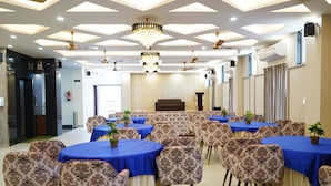 Un salón de conferencias con mesas redondas, sillas con estampado floral y un candelabro.
