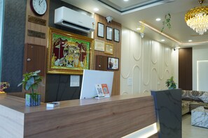 Un mostrador de recepción con un reloj, equipo de aire acondicionado, certificados enmarcados y un detalle decorativo en la pared.