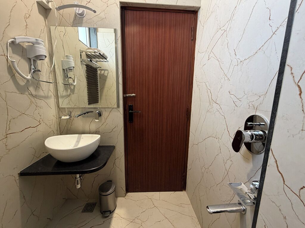 Een badkamer met een marmeren wand, een houten deur, een wit wastafelmeubel en een douchehoek.