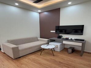 Una sala de estar moderna con un sofá, una mesa de centro, un televisor de pantalla plana montado en la pared, una mesita auxiliar y un mueble con una cafetera.