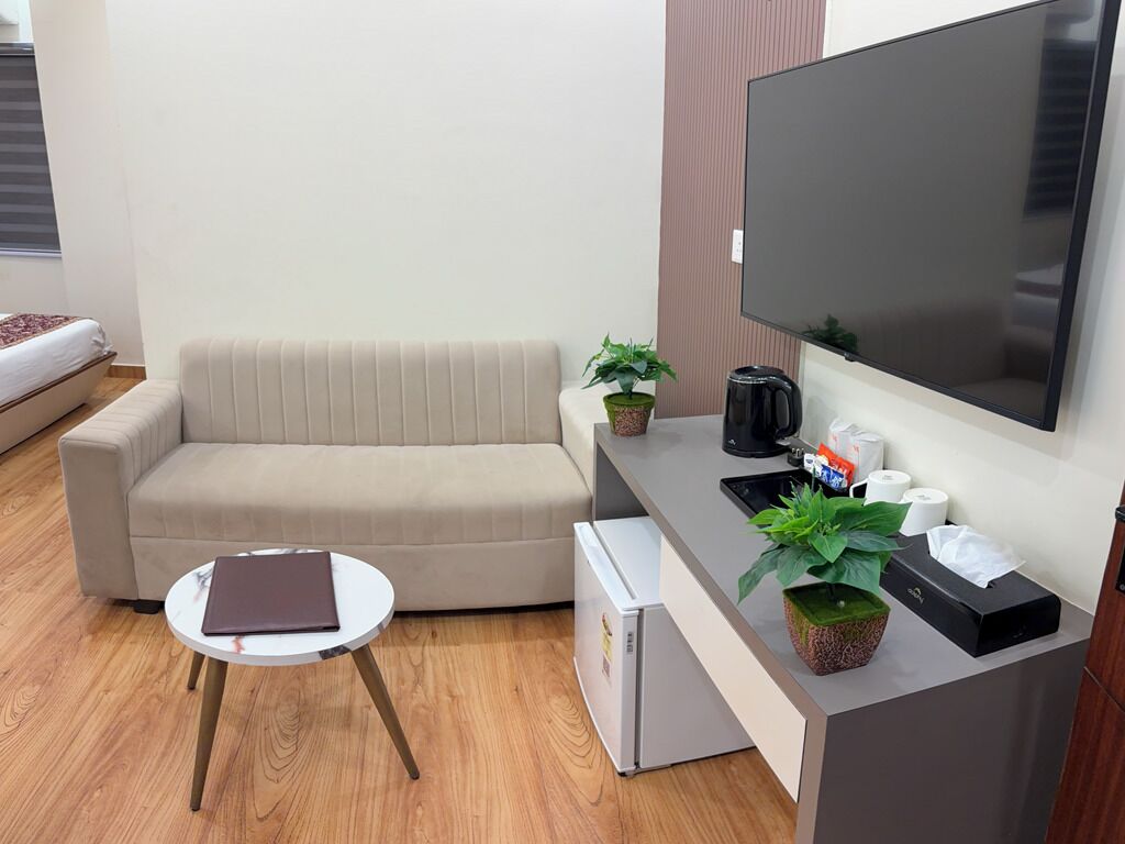 A modern living room with a sofa, a small table, a flat-screen TV, a coffee maker, and a refrigerator.