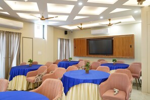 Un salón de conferencias con varias mesas, sillas, ventiladores de techo y un televisor de pantalla plana montado.