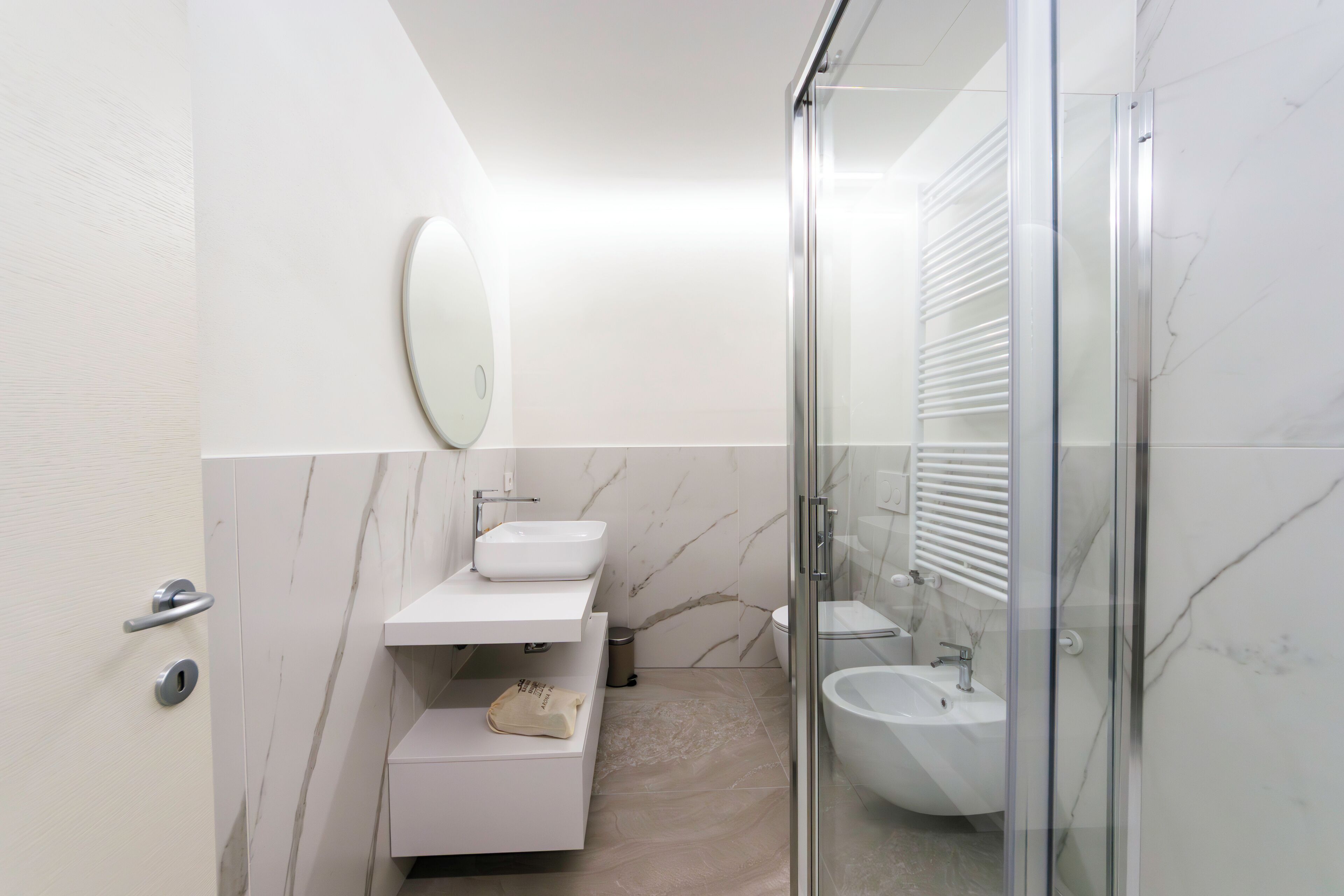Un baño moderno con ducha envuelta en vidrio, un lavamanos blanco y un revestimiento de mármol.
