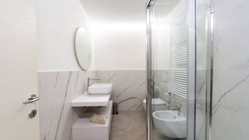 Un baño moderno con ducha envuelta en vidrio, un lavamanos blanco y un revestimiento de mármol.