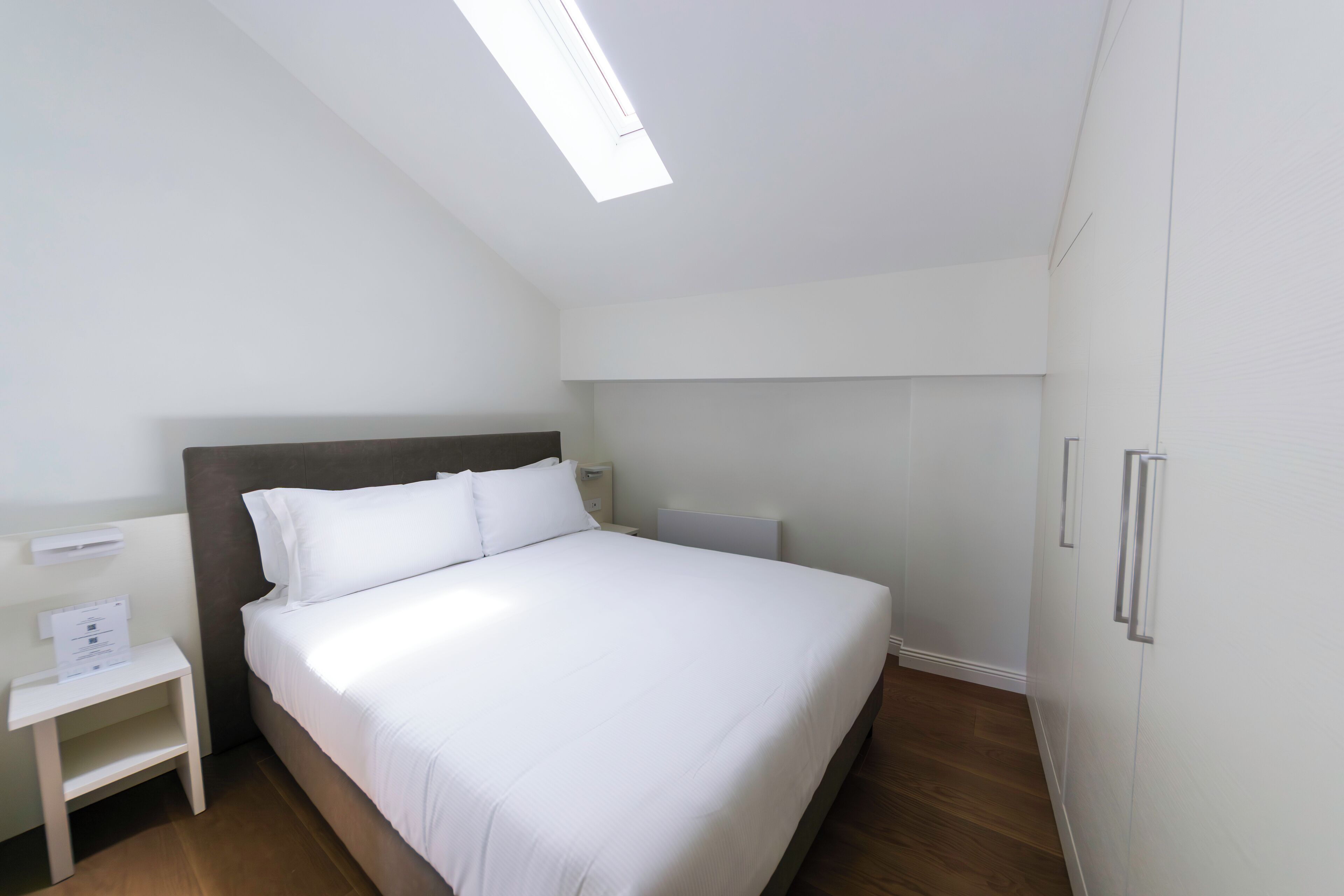 Ein modernes Hotelzimmer mit einem großen Bett, einem Nachttisch, einem Schrank und einer Kommode.