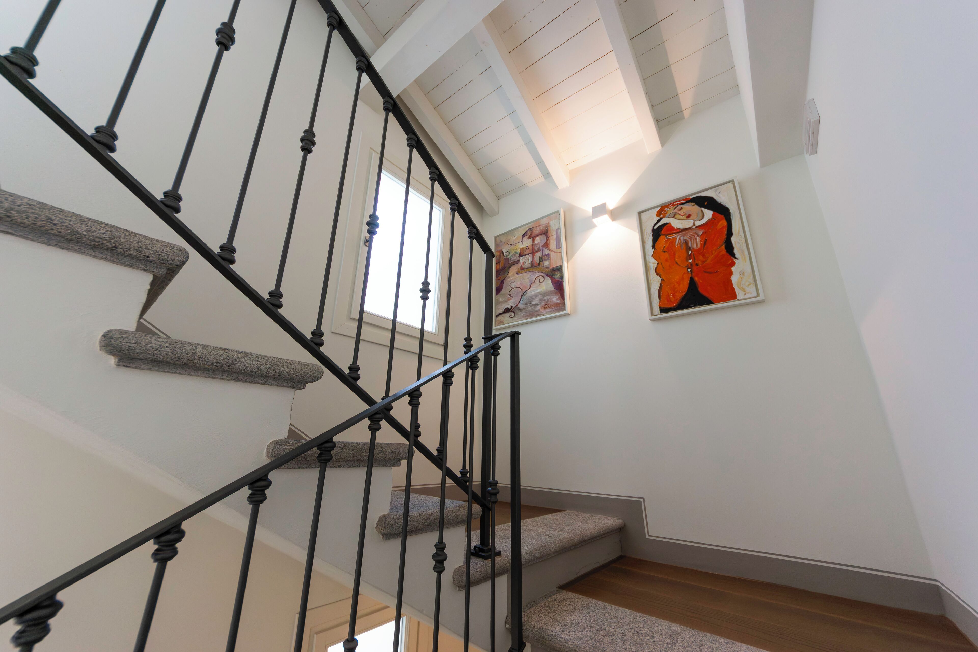 A staircase with a black metal railing, wooden steps, and a painting on the wall.