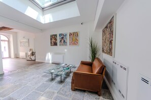 A spacious living area with a high ceiling, a glass coffee table, a brown leather sofa, and artwork on the walls. - Arona Palace - Superior Apartments (Arona)