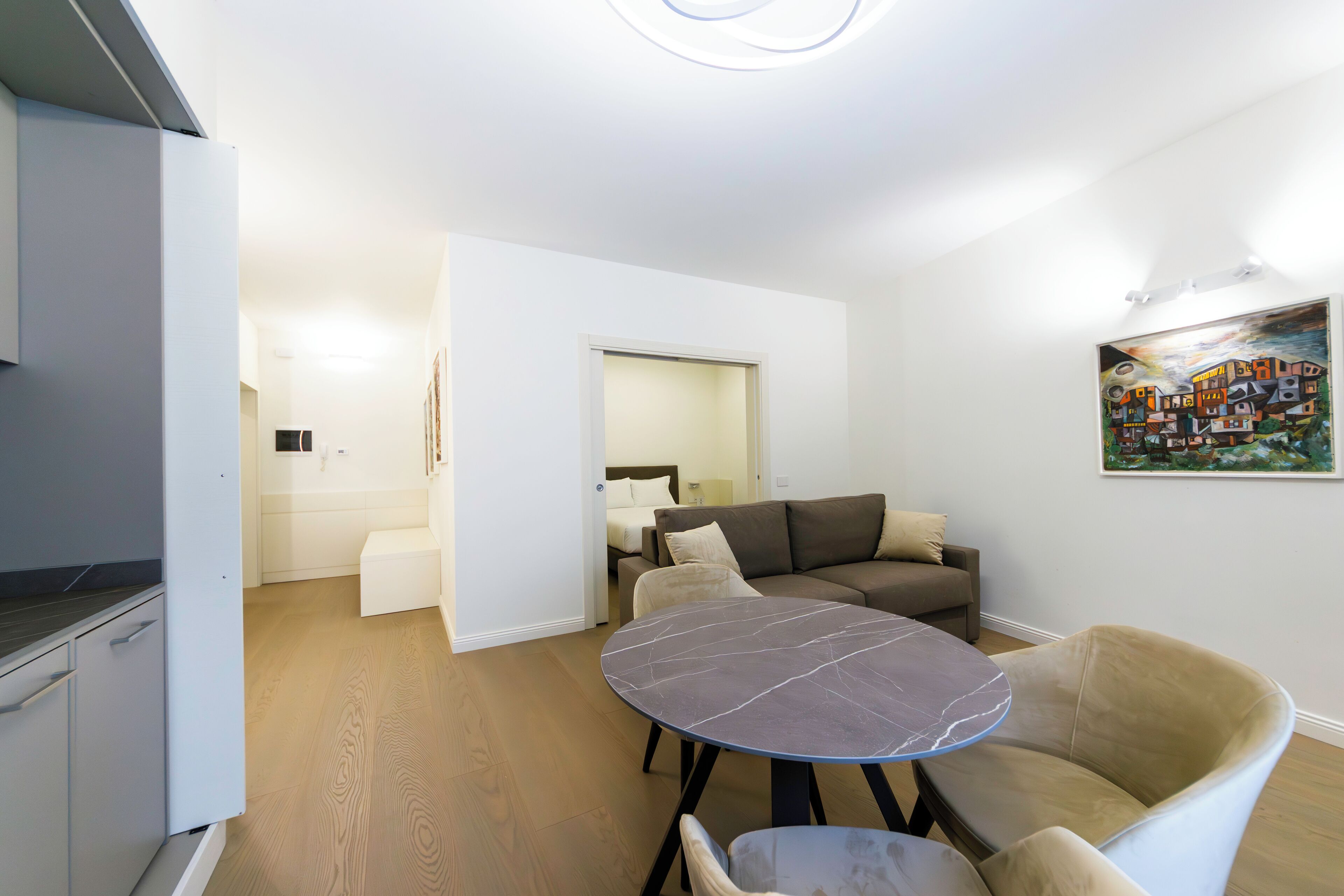 A modern living room with a round marble table, a sofa, and a kitchen area with white cabinets.
