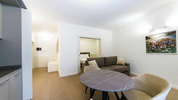 A modern living room with a round marble table, a sofa, and a kitchen area with white cabinets.