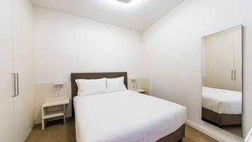 A bedroom with a single bed, a nightstand, a bedside table, and a large mirror.