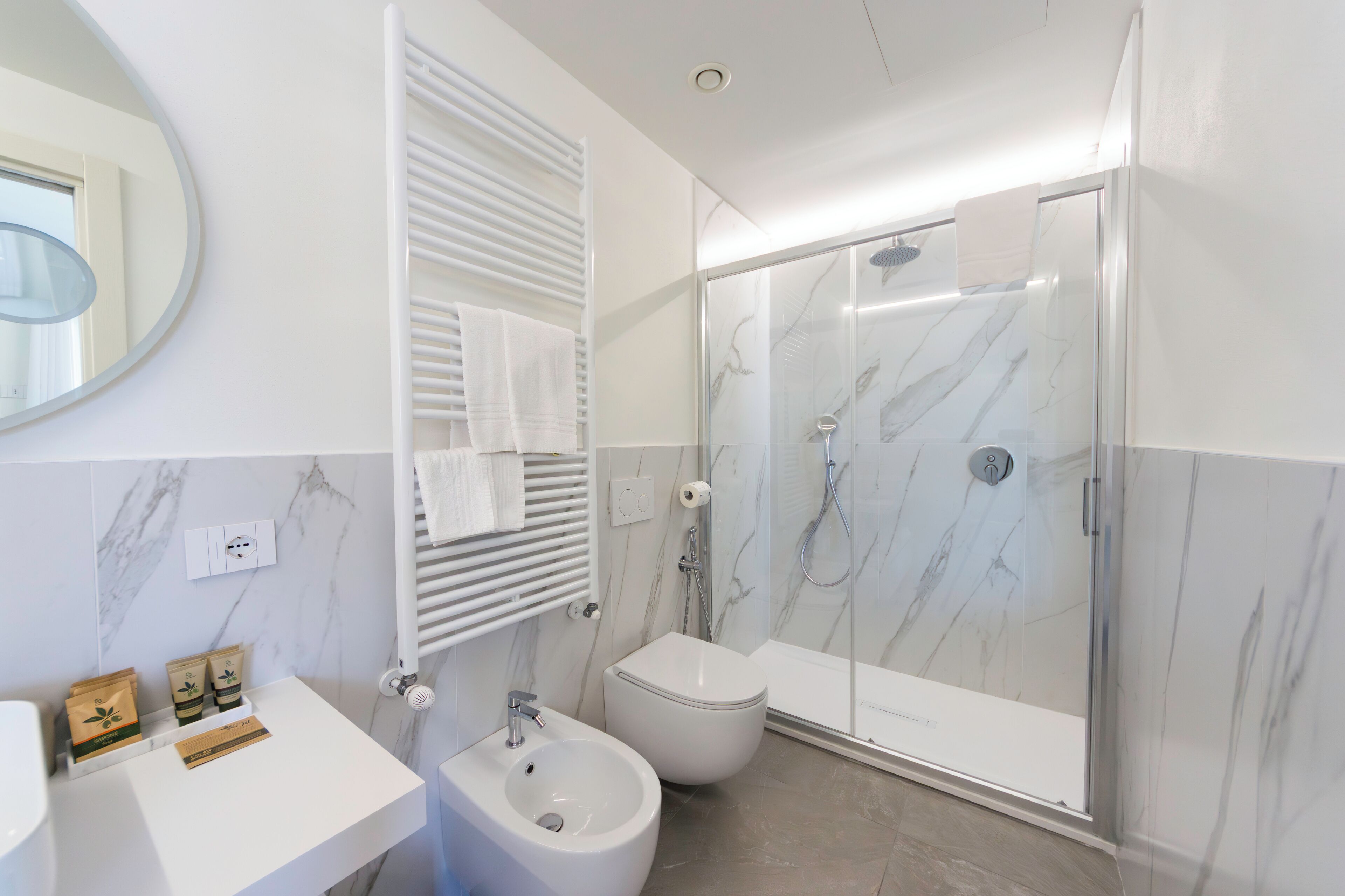 Une salle de bain moderne avec une douche en marbre, un bidet et un lavabo blanc.