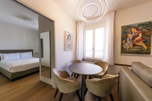 Una habitación de hotel moderna con una cama, una mesa de comedor con sillas, un sofá, un cuadro y un amplio ventanal con cortinas.