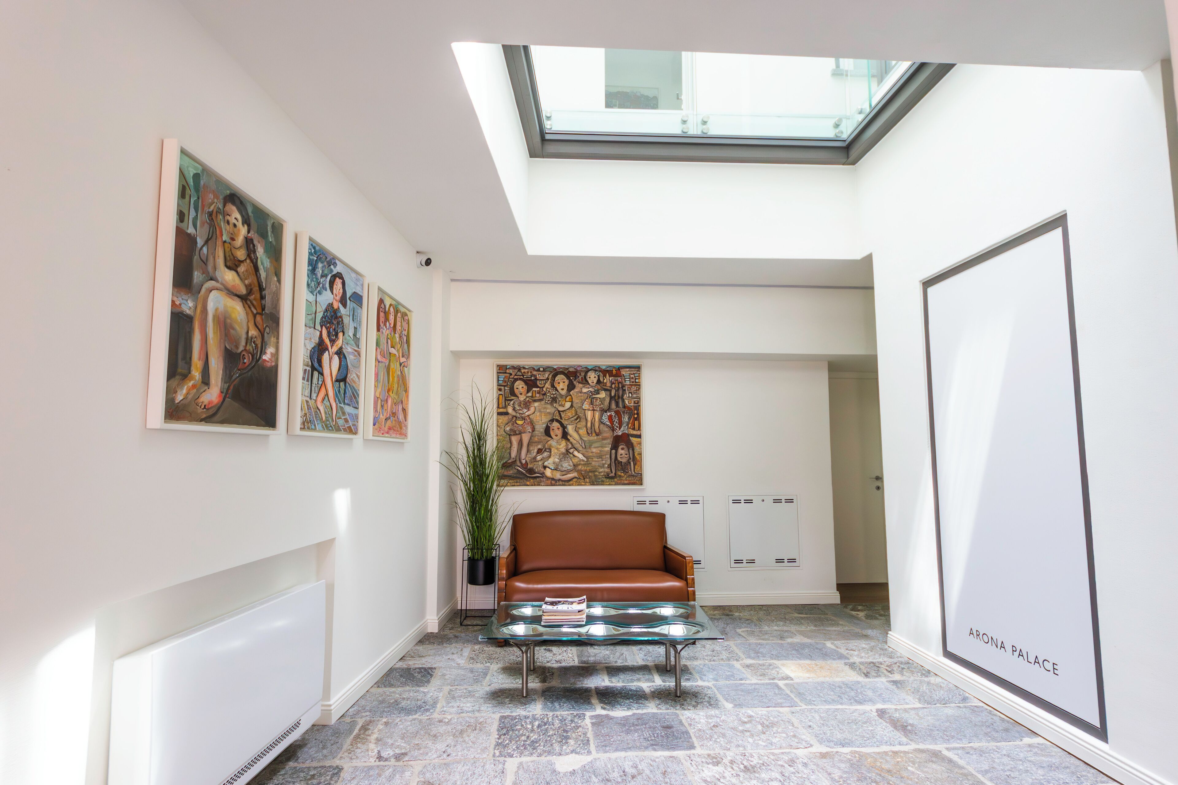 A modern interior with a glass coffee table, a brown leather sofa, and artwork on the walls.