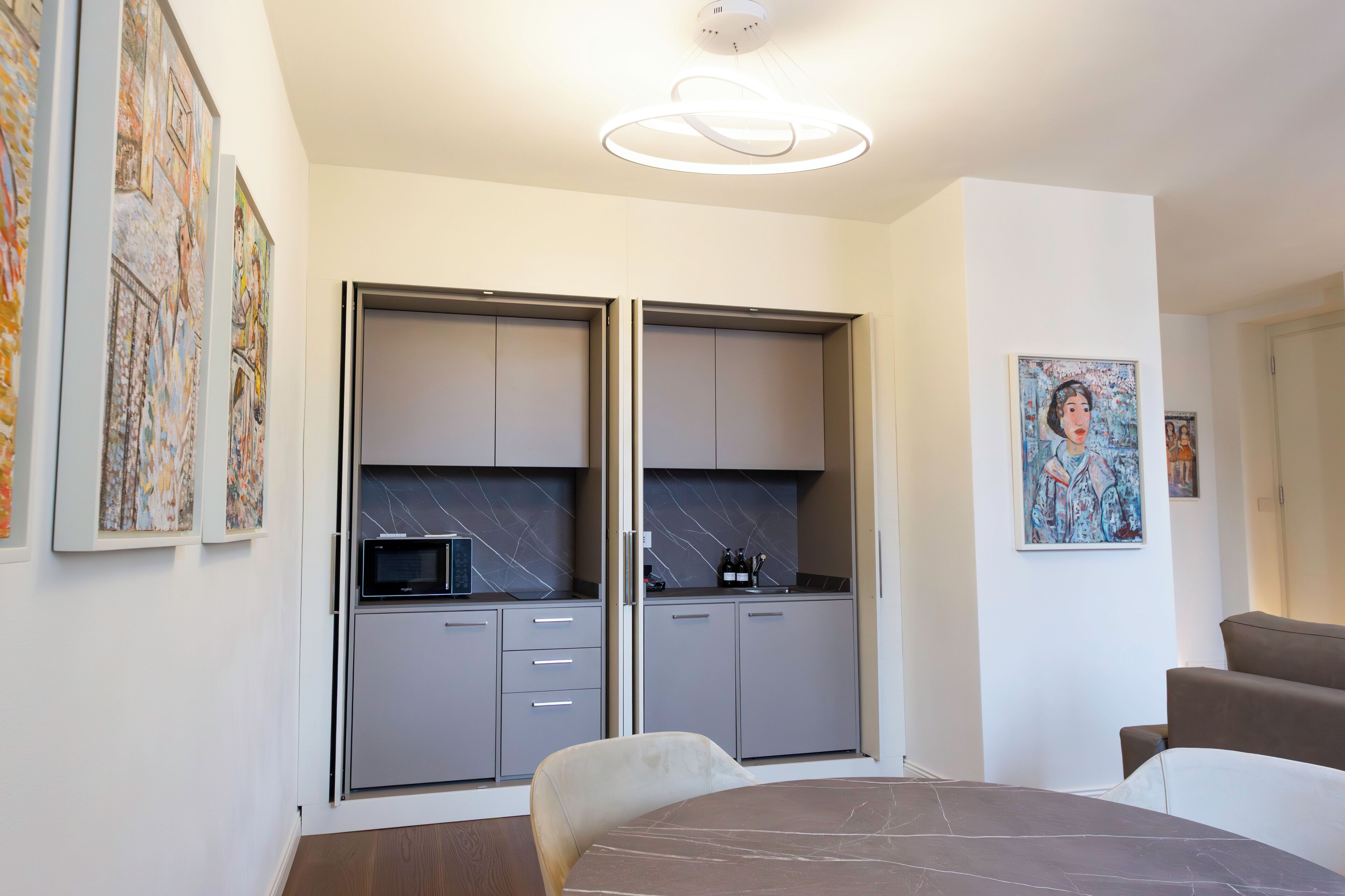 A modern kitchen with grey cabinets, a built-in microwave, and a dining area with a marble table and chairs.