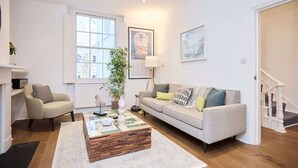 Uma sala de estar com sofá, poltrona, mesa de centro e escada.