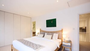 Quarto moderno com uma cama grande, mesas de cabeceira, um quadro verde e um guarda-roupa.