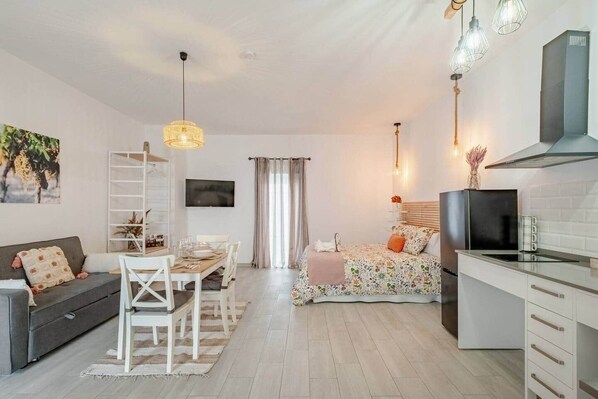 Una sala moderna con sofá, mesa de comedor y sillas, una cocina con estufa y armarios, y un dormitorio con cama y cortinas.