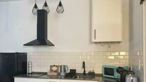 A compact kitchen with white cabinets, a black range hood, a sink, and a microwave.