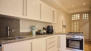 A modern kitchen with white cabinets, a granite countertop, a built-in oven, and a coffee maker. - The West Kensington Hideout (Greater London)