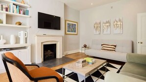 A modern living room with a fireplace, a sofa, a coffee table, and a TV mounted on the wall. - The West Kensington Hideout (Greater London)
