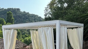 Ein weißes Himmelbett mit Vorhängen, ein Holztisch und ein Stuhl auf einer Holzterrasse.