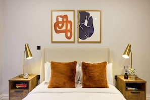 Una cama bien hecha con dos almohadas marrones, un cabecero de madera y dos mesitas de noche con lámparas y libros.