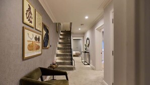 A hallway with a staircase, a chair, and framed artwork on the wall.