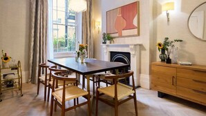 A dining area with a table, chairs, a fireplace, a wall-mounted lamp, and a window with curtains.