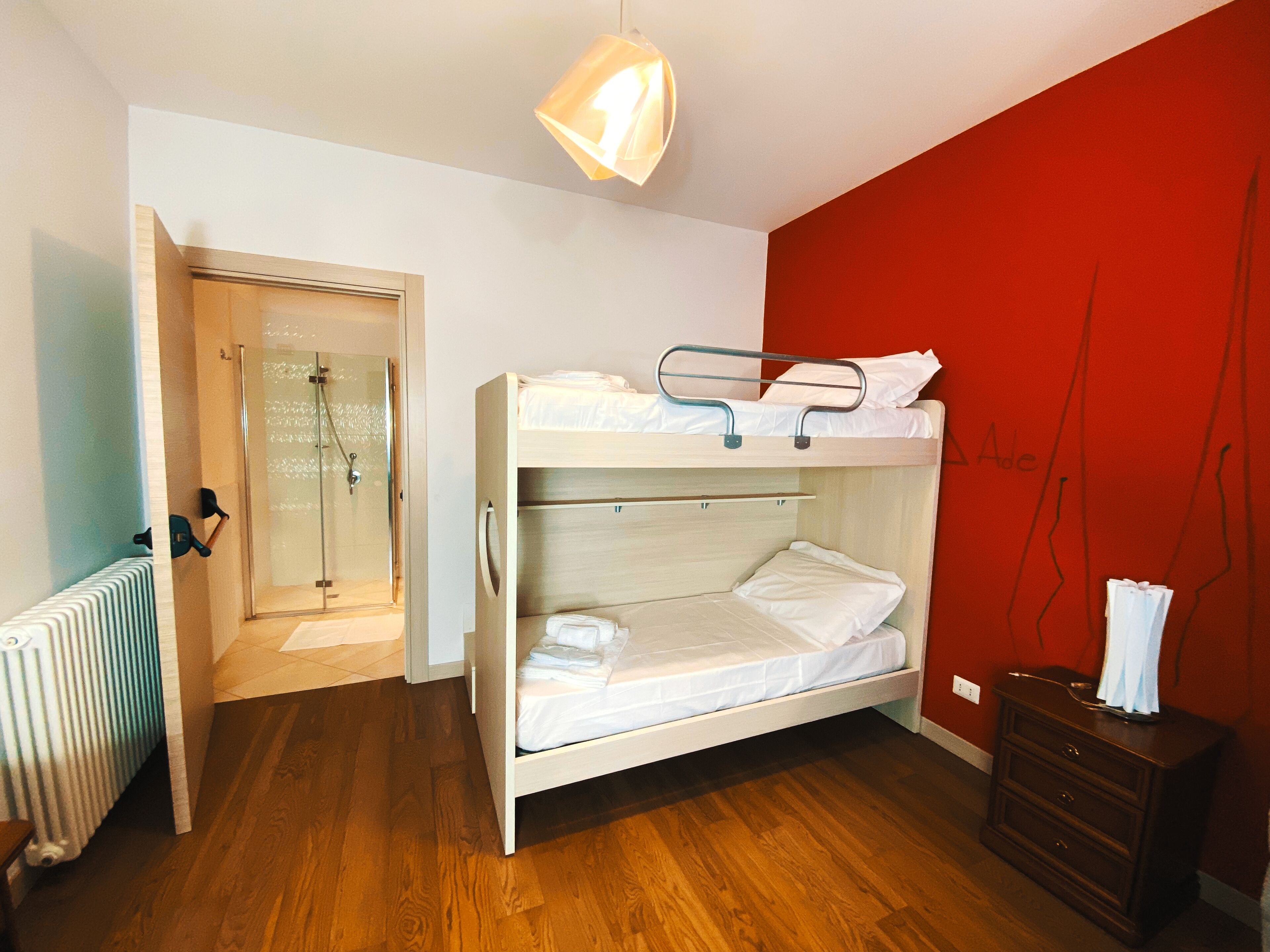 Una cama litera con cabecera de madera, un radiador, suelo de madera y una pared de acento roja.