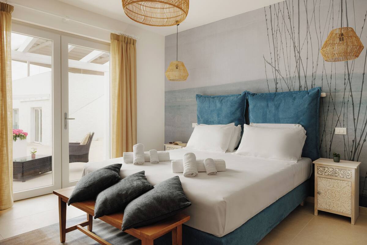 A modern bedroom with a large bed, a wooden bench, and a nightstand with a lamp.